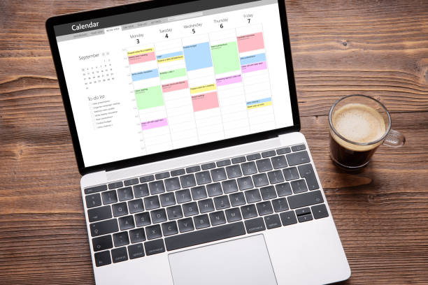 Top view of laptop with calendar app on screen filled with different weekly appointments, meetings and tasks: Weekly Scrum Meeting!