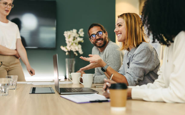 Business woman talking to her colleagues during a meeting in a boardroom. Group of happy business people working together in a creative office. Meeting Check-In Questions